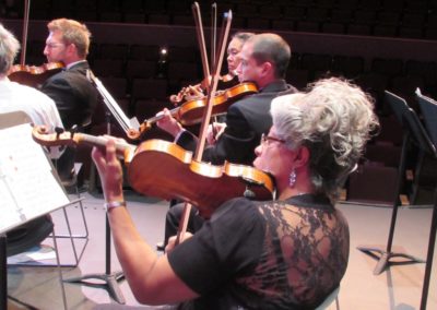 A group of people playing violins in a concert hall as part of the SoCal Philharmonic.