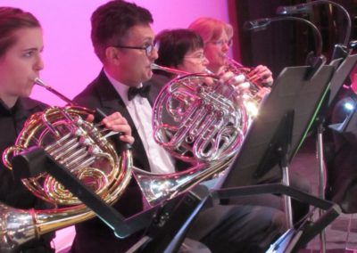 A group of people in tuxedos playing french horns at SoCal Philharmonic.