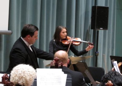 A man in a suit and tie is playing a violin for the SoCal Philharmonic.