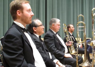 Members of the SoCal Philharmonic in tuxedos posing with a trombone.