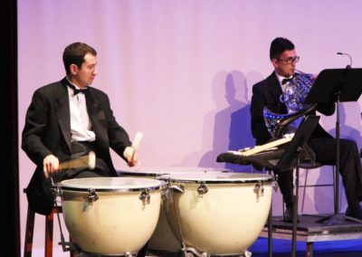 Two men in tuxedos playing drums on stage as part of the SoCal Philharmonic.