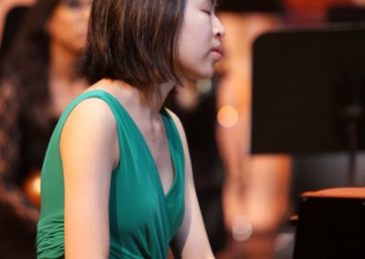 A woman playing the piano in a green dress at a SoCal Philharmonic performance.