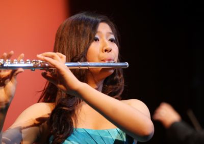 A young woman playing the flute in front of the SoCal Philharmonic audience.